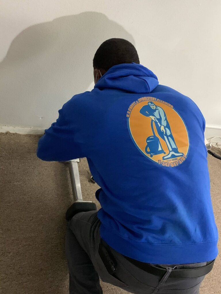 Technician from KG Carpet and Upholstery Cleaning Corp performing professional carpet extraction in a residential room.
